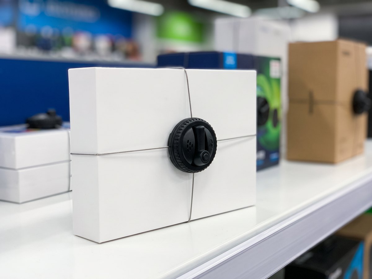 White electronics box protected by a round anti-theft tag with crossed steel cables